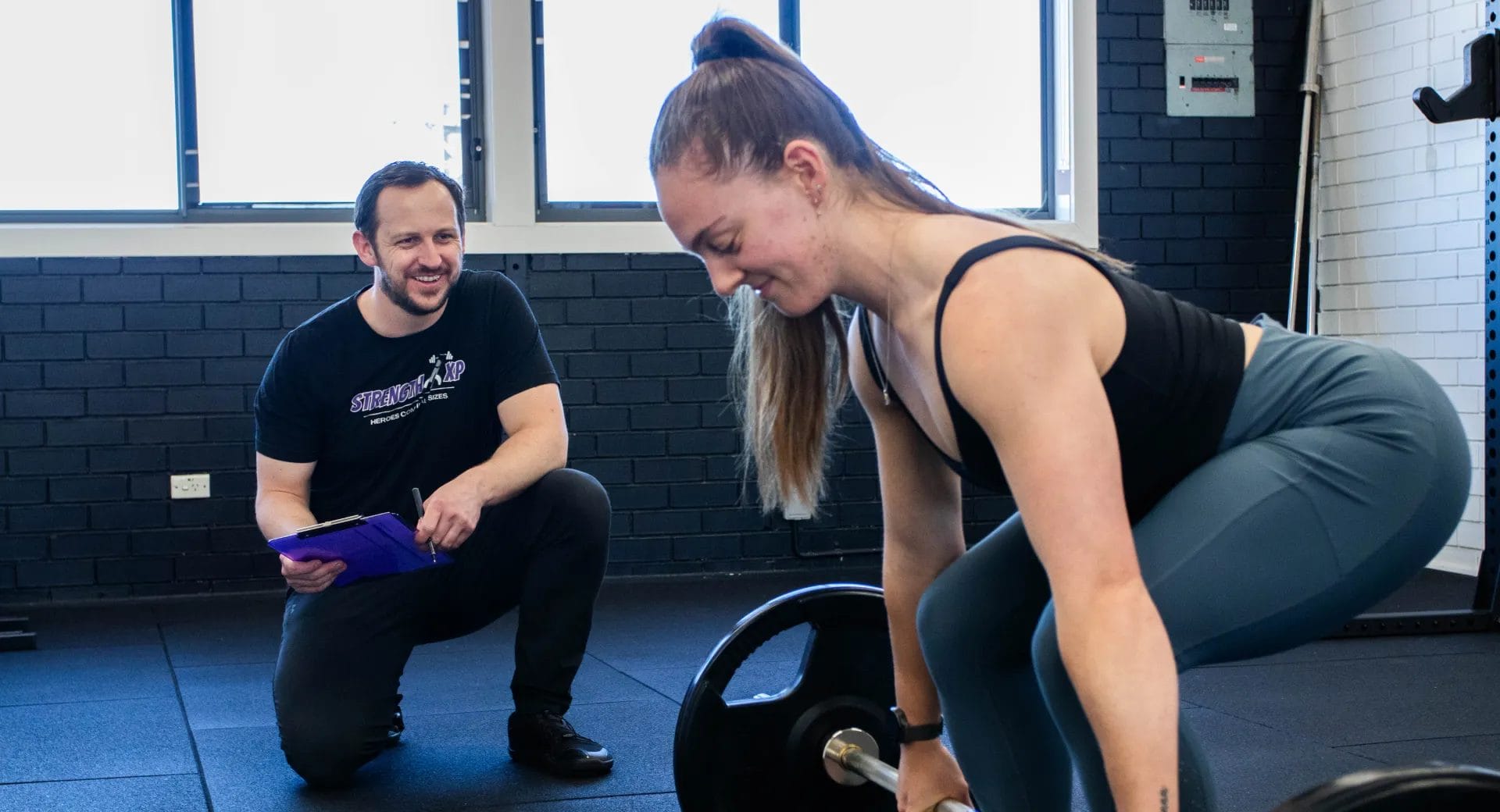 Woman lifting a barbell with assistance from a trainer